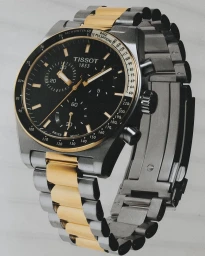 Close-up product shot of a Tissot chronograph watch with a black dial and two-tone steel and gold bracelet.