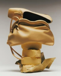 Stacked butter blocks supporting a leather handbag and flat shoe against a neutral grey studio background.