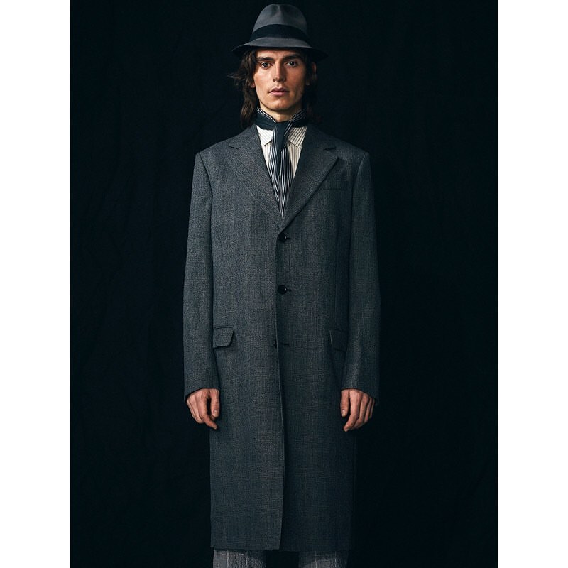 Portrait of a man in a gray wool coat and hat, featuring a dark background, studio lighting, and a classic, elegant fashion style.