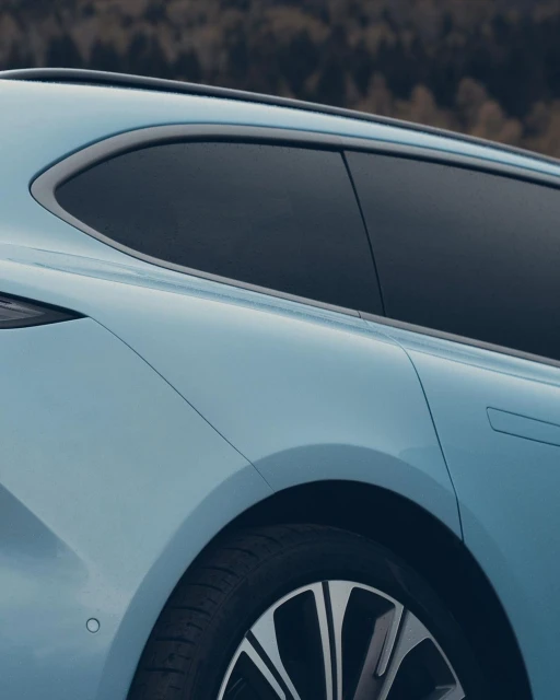 Close-up of the back of a light blue car with dark tinted windows and a view of the wheel against a dark background.