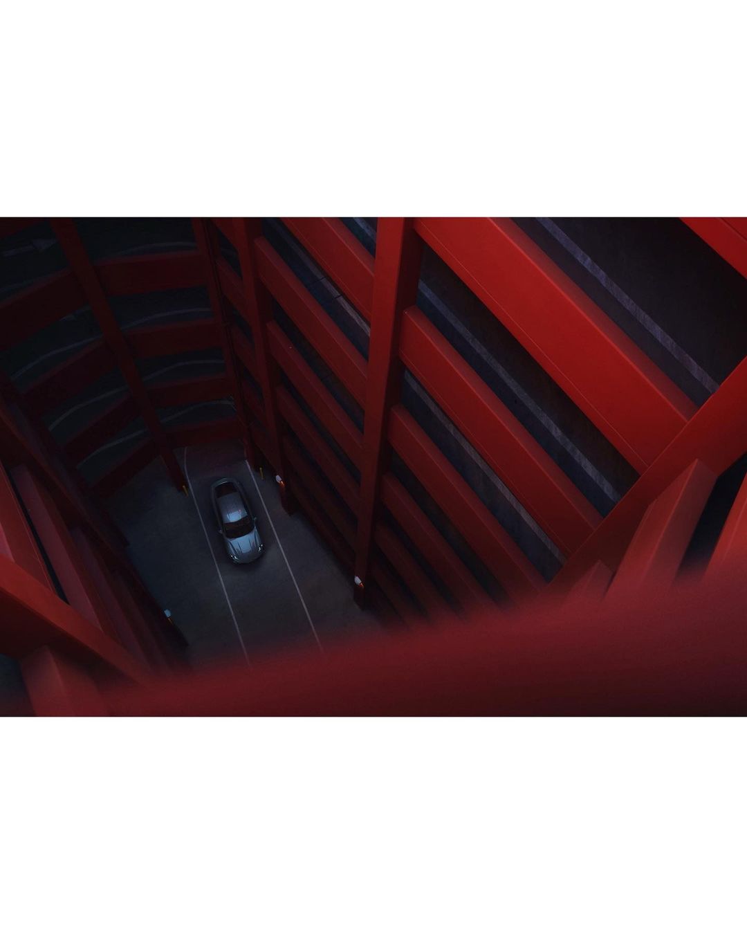 A car driving through a red tunnel, shot from above to highlight the structure and vehicle in a symmetrical composition.