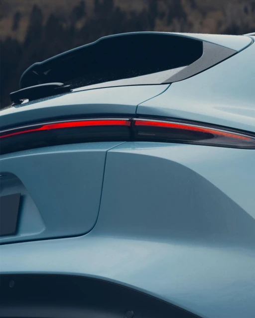 Close-up shot of the rear of a light blue crossover SUV with red tail light against a blurred, dark woodland background.