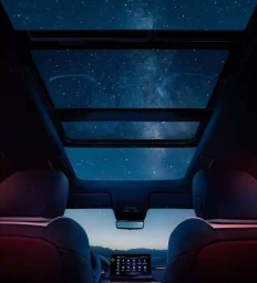 Looking up through a car panoramic sunroof at a starry night sky with mountains visible on the horizon