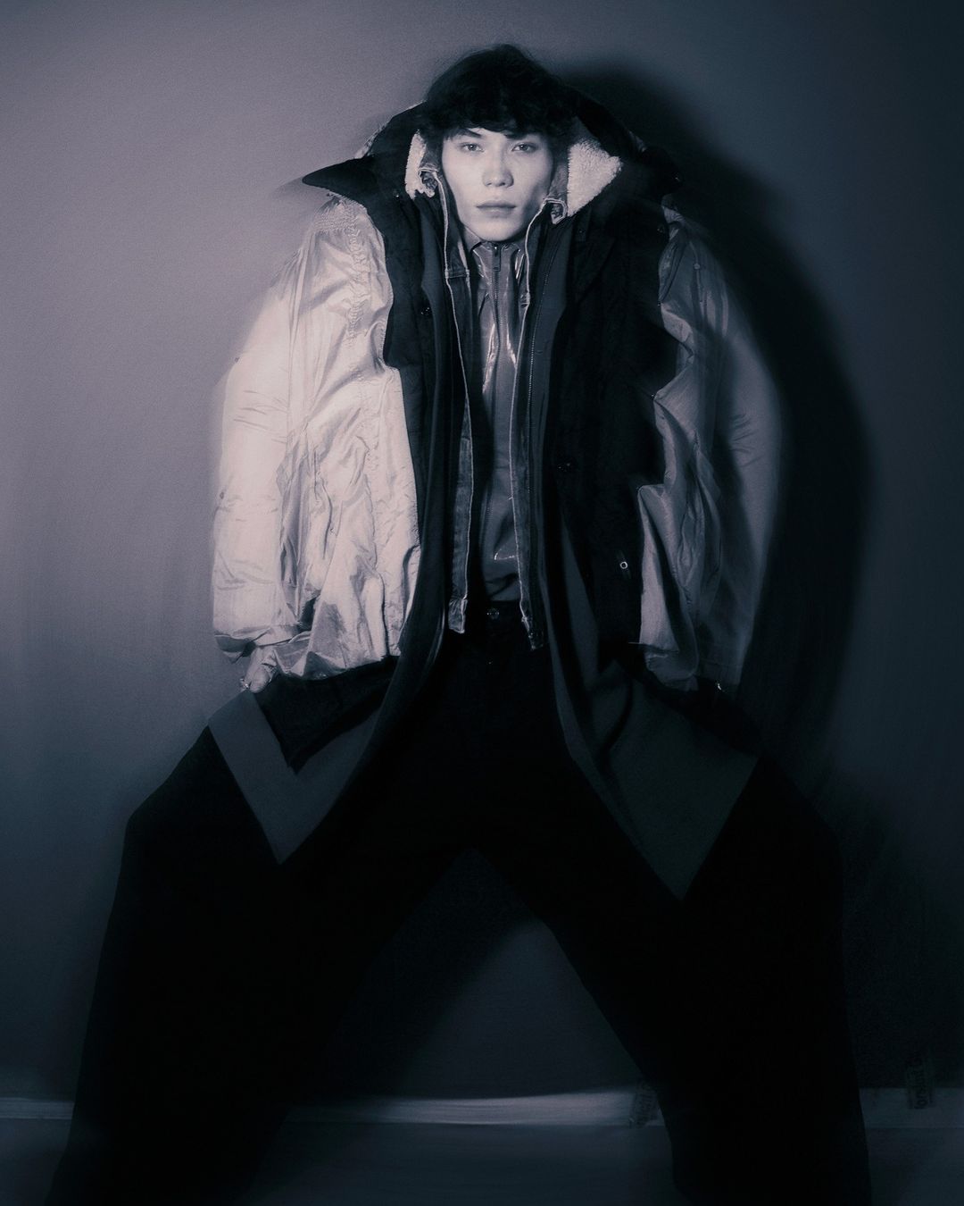 Model wearing layered oversized winter jackets and dark trousers against a plain dark studio background