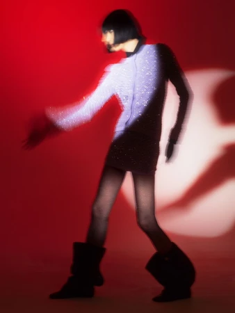 Motion-blurred model wearing a sparkly top and dark boots against a vibrant red background in Berlin by photographer Osman Özel.