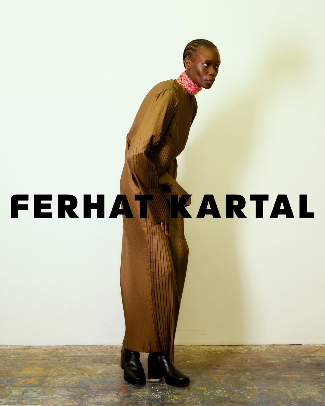 Runway fashion shot showcases a Black woman in a brown pleated dress and black boots, accented by Ferhat Kartal text on a white backdrop.