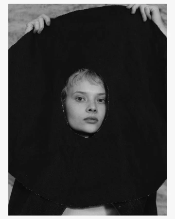 Portrait of a woman holding up a dark circular textile piece with a cutout framing her face, photographed by Osman Özel.