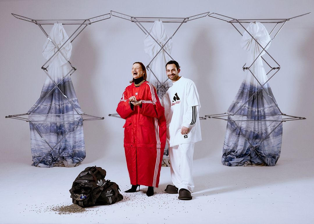 Two adults in Adidas apparel strike a pose amidst abstract clothing racks and scattered seeds in a bright, white studio setting.