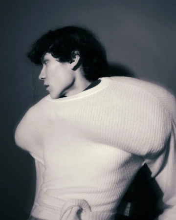 Monochromatic portrait of a young adult with dark hair wearing a white sweater, looking left, in a studio setting.