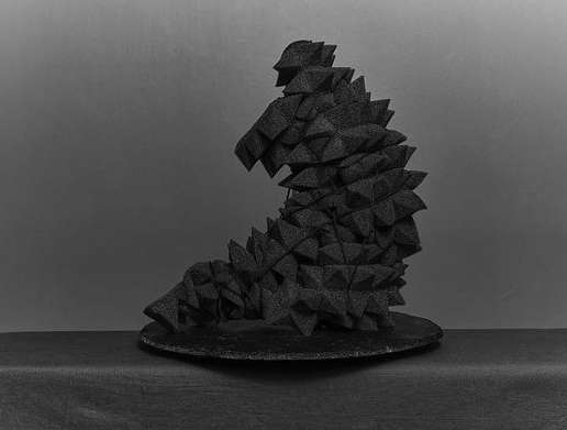 Abstract geometric sculpture made of black foam triangles, creating a textured, organic form against a gray backdrop.