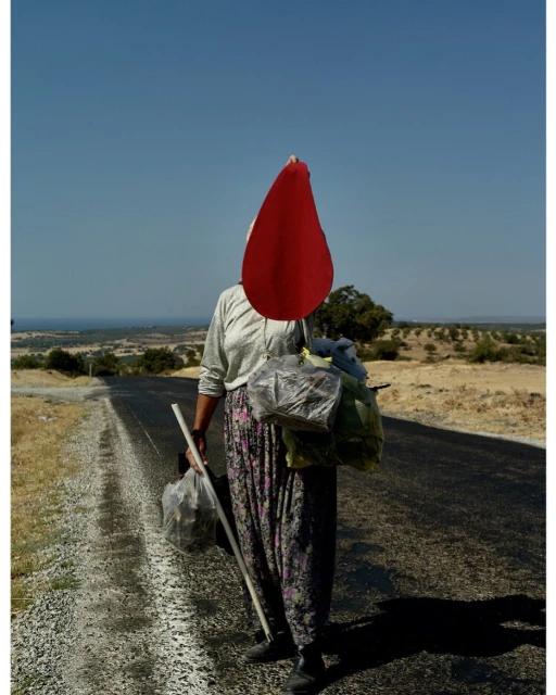 Woman with packages walks on road under blue sky on sunny day. Rural landscape and clear skies compose background. Walking stick in hand.