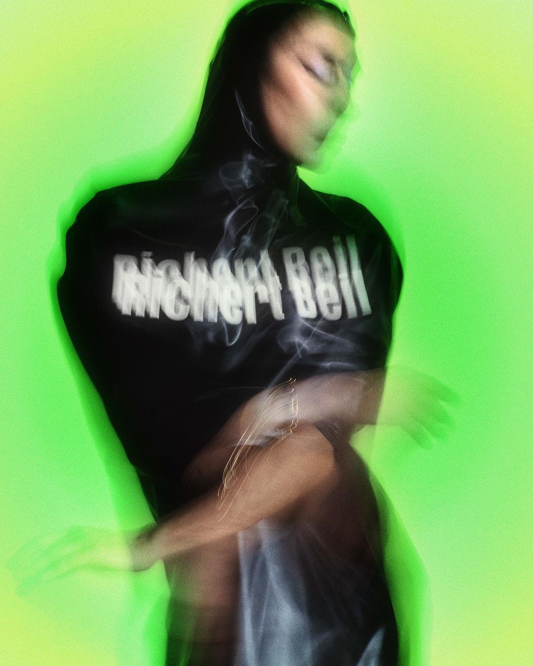 Woman in black top posing against a green screen, motion blur effect applied; the text on the shirt reads Richard Bell in white.