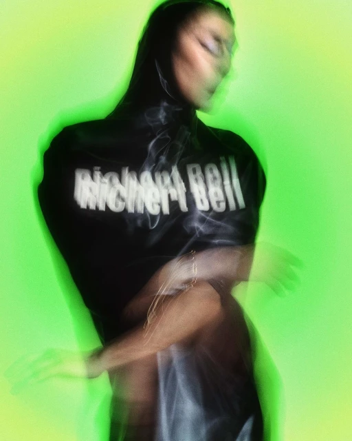 Woman in black top posing against a green screen, motion blur effect applied; the text on the shirt reads Richard Bell in white.