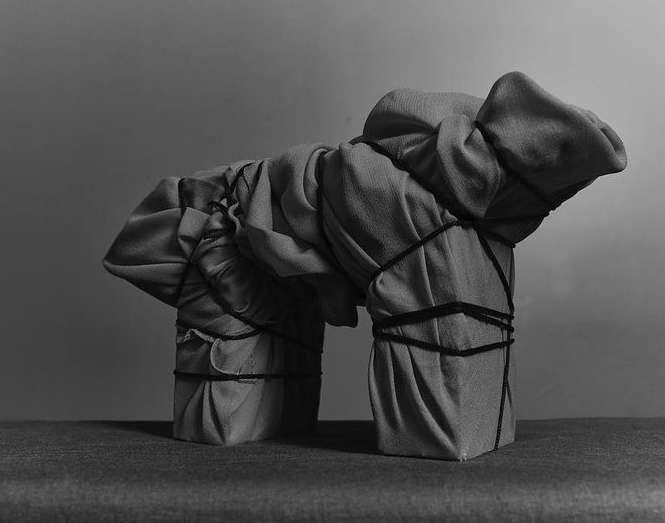 Abstract studio shot of geometric sculpture of draped fabric tied with string in shades of gray, creating a tactile visual.