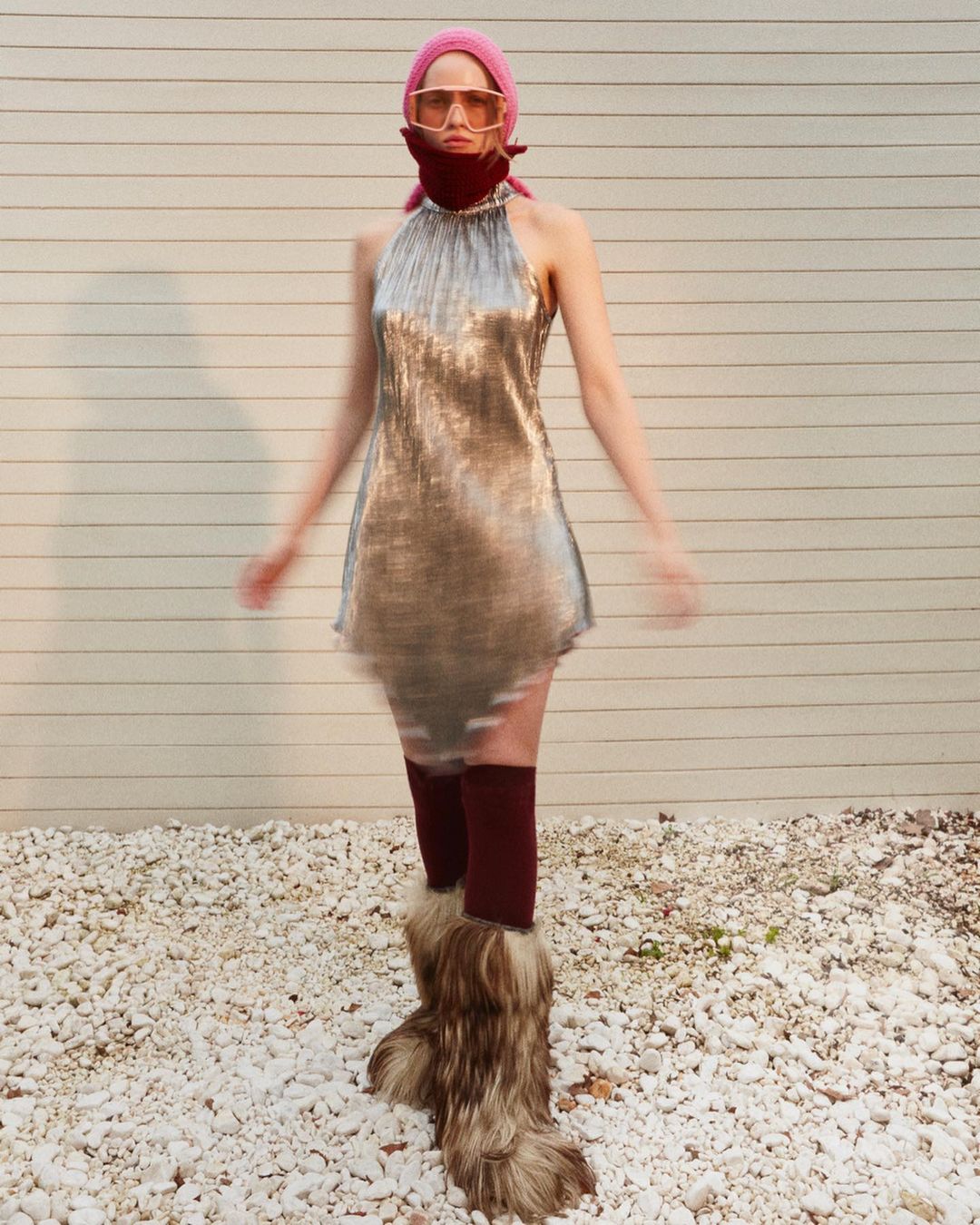 Full shot of a woman in a silver dress and fur boots in an outdoor setting, wearing sunglasses and a headscarf, showcasing a fashion-forward look.