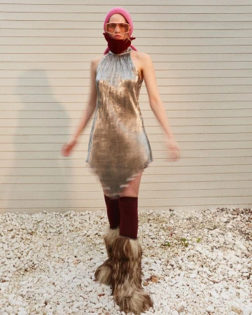 Full shot of a woman in a silver dress and fur boots in an outdoor setting, wearing sunglasses and a headscarf, showcasing a fashion-forward look.