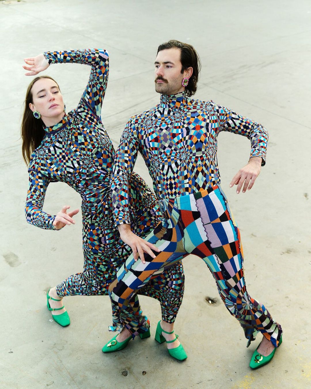 Two people in colorful geometric patterned outfits strike a pose outdoors. A woman and a man wearing fashionable clothing.