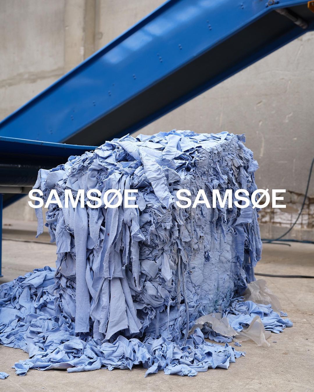 Bale of light blue fabric scraps with conveyor belt overhead, creating a visual study in texture and monochromatic color.