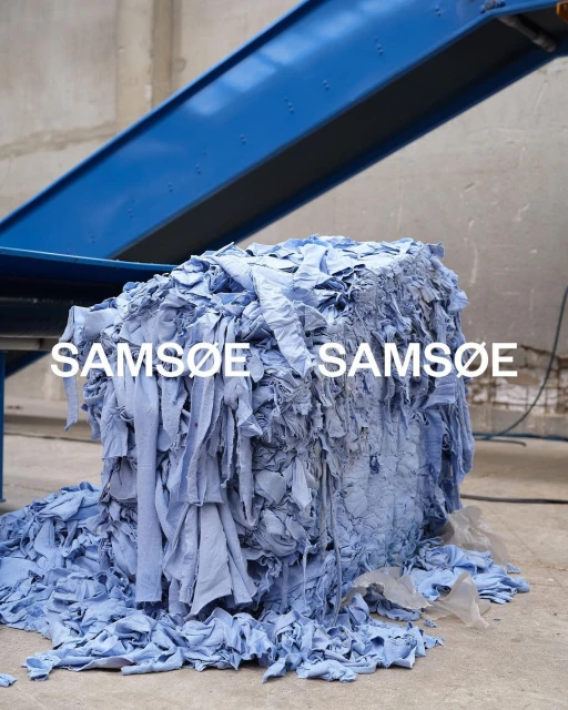 Bale of light blue fabric scraps with conveyor belt overhead, creating a visual study in texture and monochromatic color.
