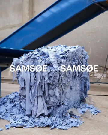 Bale of light blue fabric scraps with conveyor belt overhead, creating a visual study in texture and monochromatic color.