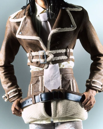 Fashionable adult in a brown shearling aviator jacket with a dress shirt and tie, posing in a studio setting with neutral lighting.