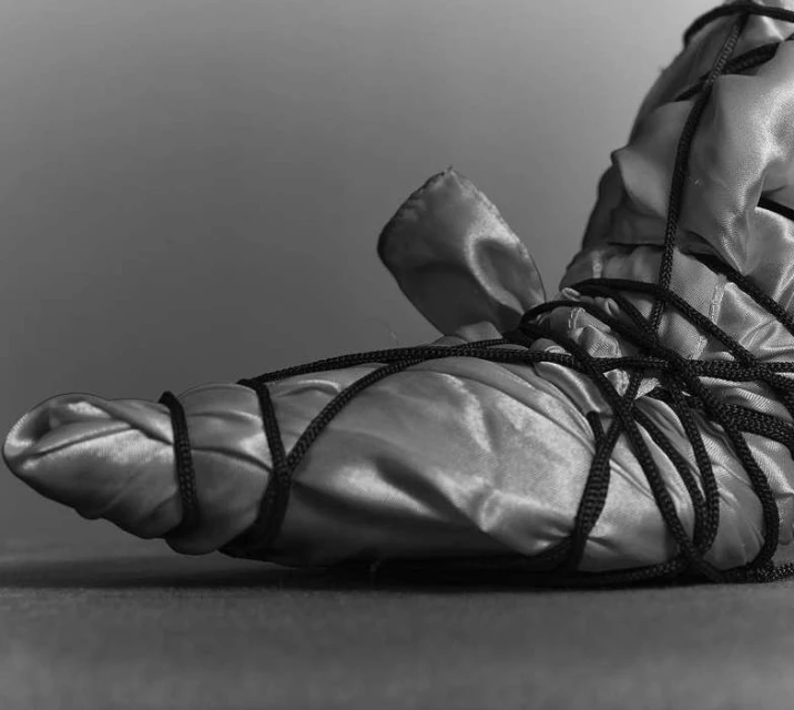 Monochrome studio image of a satin-covered bundle secured with black cord, creating abstract forms and strong contrast against a plain backdrop.