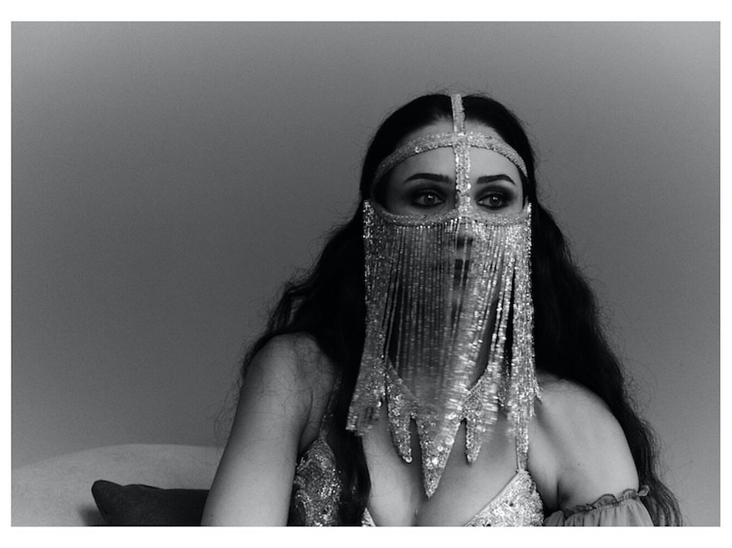 Woman wearing an elaborate beaded fringe face veil and metallic dress photographed in monochrome by Osman Ozel.