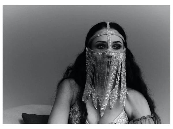 Woman wearing an elaborate beaded fringe face veil and metallic dress photographed in monochrome by Osman Ozel.
