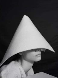Model wearing a large white conical hat pulled down over eyes, captured in portrait by Osman Özel.