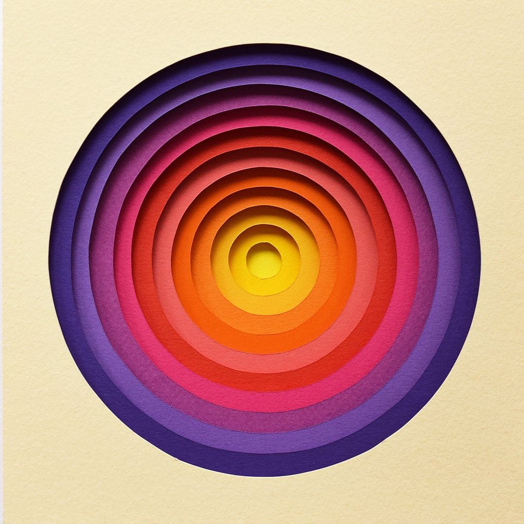Abstract art of concentric circles made of paper layers with yellow, orange, red, pink, and purple in a square ivory frame.