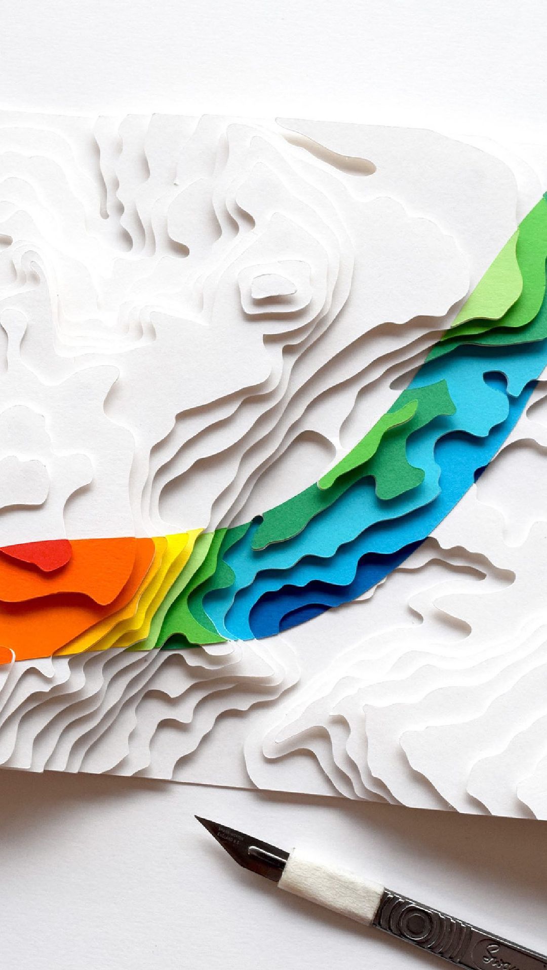 Elevated view of a paper art topography model with layers of white paper and colorful contour lines indicating the height of the terrain.