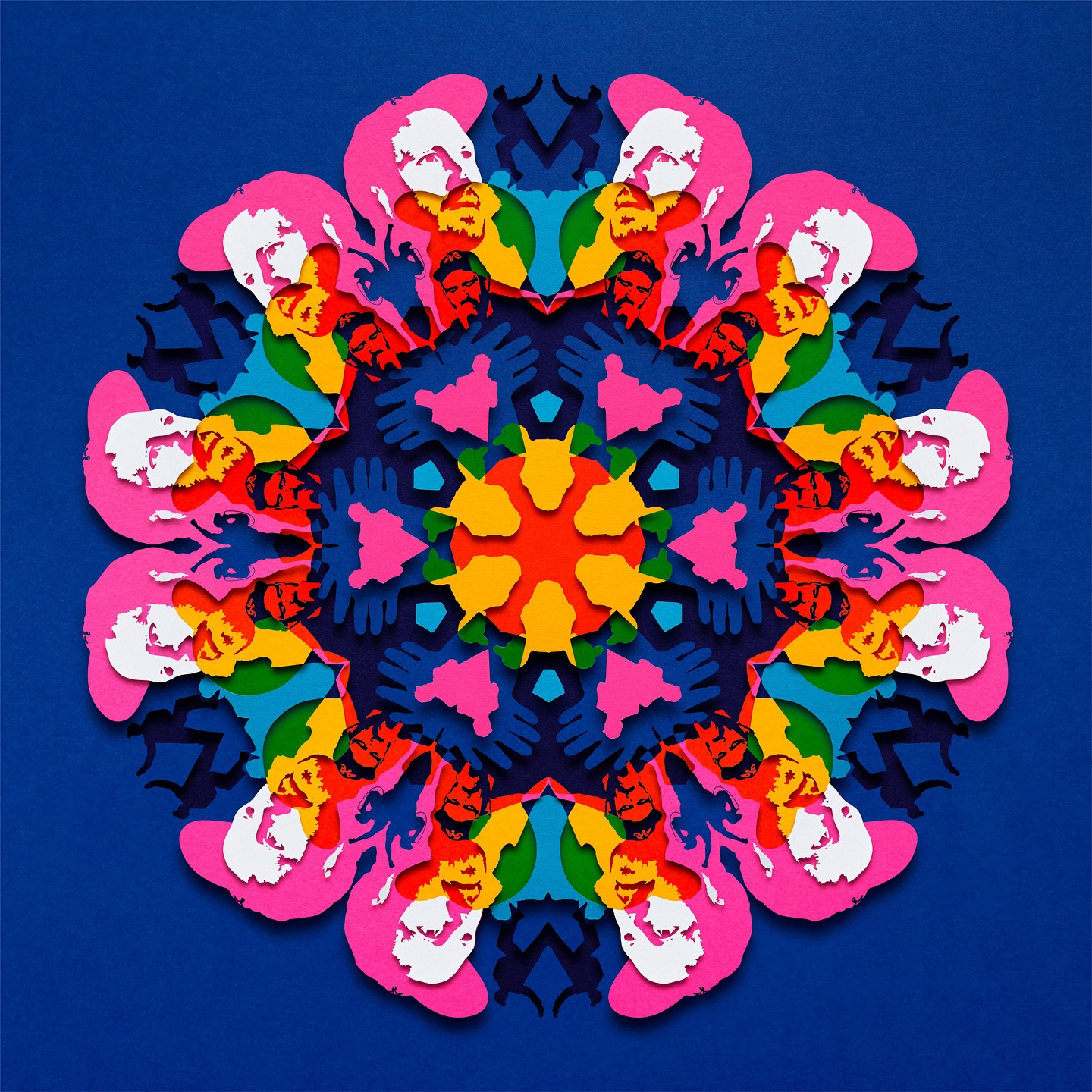 Detailed paper art mandala with symmetrical patterns of faces and geometric shapes in vivid pink, blue, green, yellow, and red on a blue background.