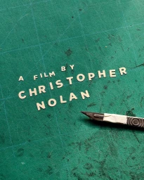 Handcrafted paper lettering that reads A Film By Christopher Nolan arranged on a green cutting mat with a craft knife
