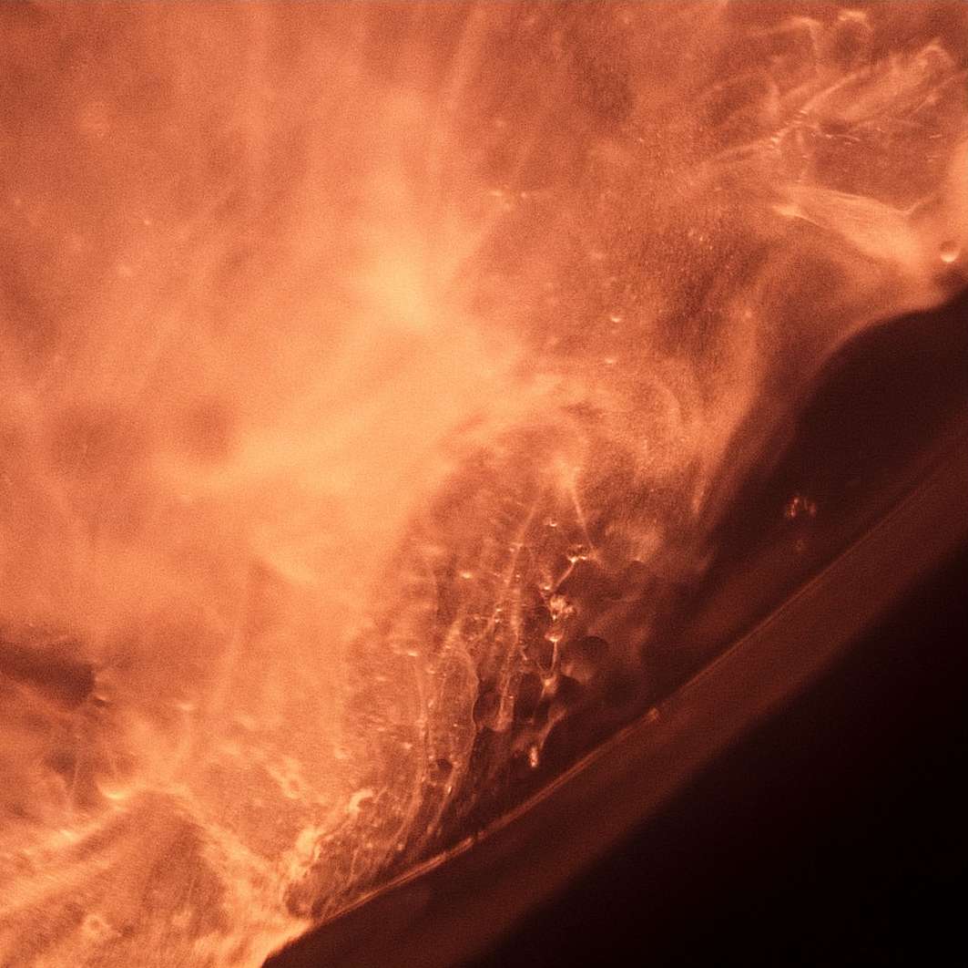 Abstract close-up of a copper-colored liquid surface with shimmering texture and light reflections, resembling a natural phenomenon.