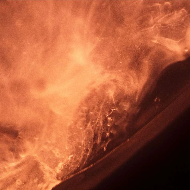 Abstract close-up of a copper-colored liquid surface with shimmering texture and light reflections, resembling a natural phenomenon.
