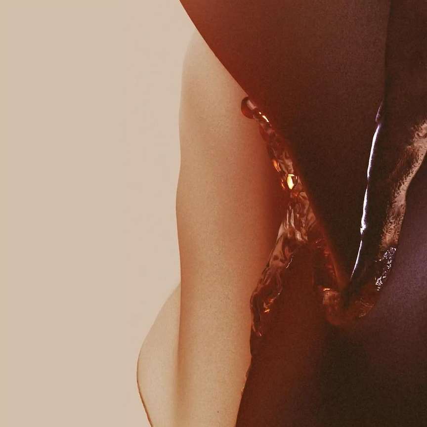 Abstract nude arm shot. Dark liquid drips over tan skin in a high-contrast studio-lit environment. Evokes beauty, health, and wellness.