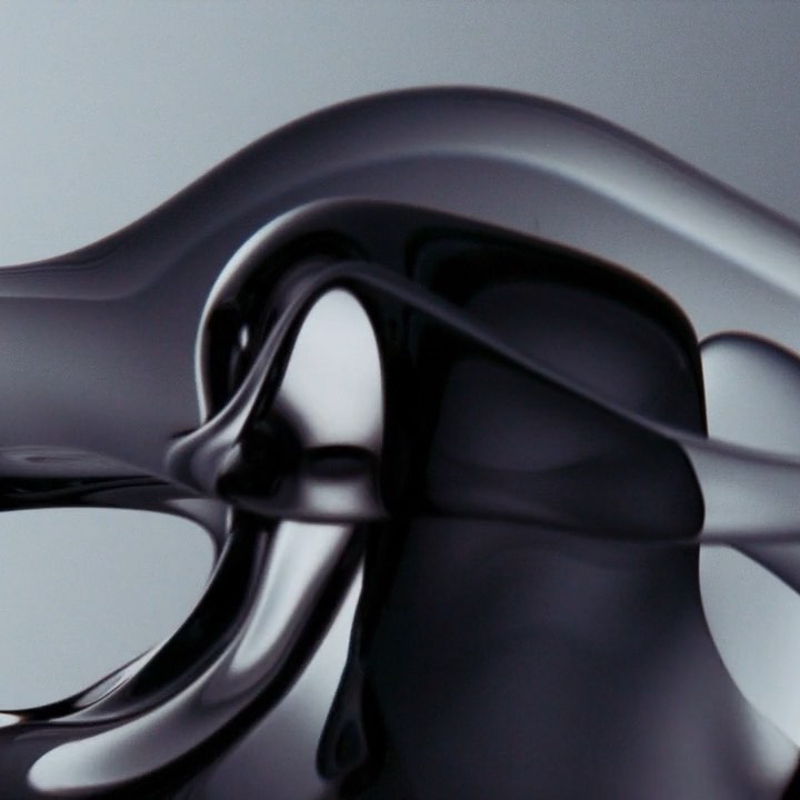 Abstract glossy black fluid forms an undulating, flowing design with smooth, reflective surfaces and a soft, diffused grey background.
