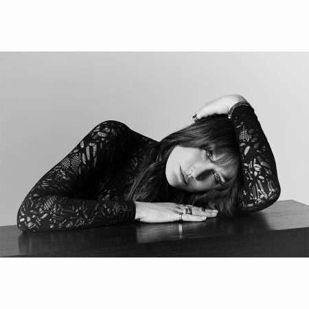 Monochrome portrait of a woman resting on a dark surface wearing a patterned black long-sleeve top by P.a Hue De Fontenay