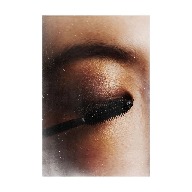 Close-up of an eye and eyebrow with mascara brush, makeup, and beauty product application in a beauty editorial shot.