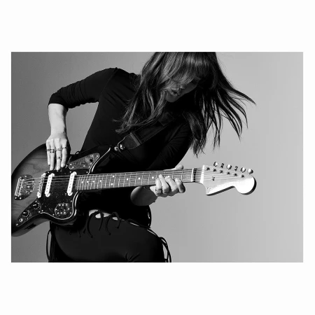 Black and white portrait of a woman playing an electric guitar against a plain light background