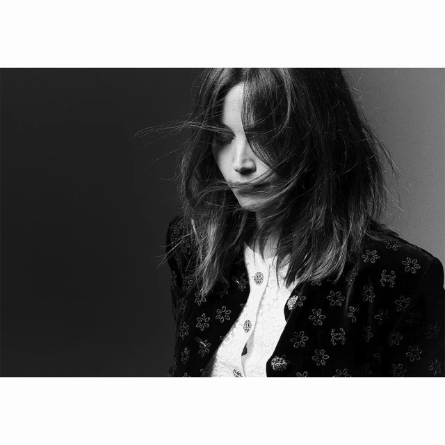 Black and white portrait of a woman with long hair wearing a floral jacket and white top, looking down in a studio setting.
