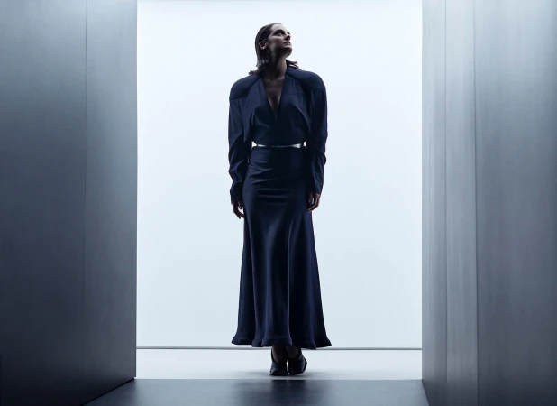 Woman in dark long-sleeve dress standing framed between architectural walls in a minimalist interior shot by P.a Hue De Fontenay