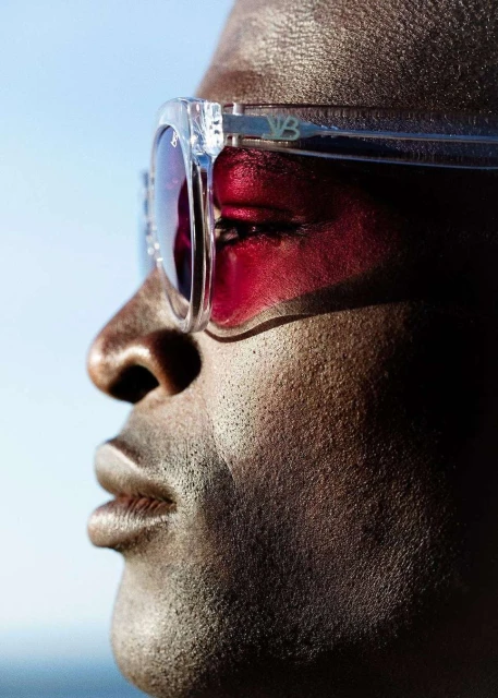Close-up of an adult man with dark skin wearing tinted sunglasses against a blue sky. Focus on face and eyewear.