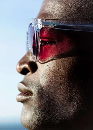 Close-up of an adult man with dark skin wearing tinted sunglasses against a blue sky. Focus on face and eyewear.