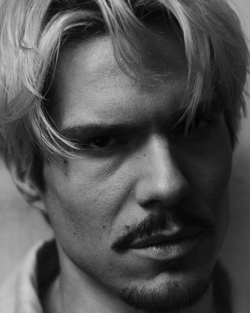 Black and white portrait of a blonde adult male with a mustache and goatee, looking directly at the camera with a serious facial expression.