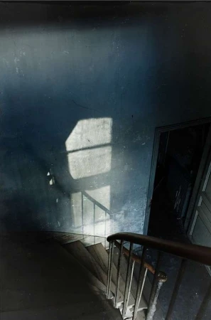 Downward view of a dark staircase with a window light projection on the textured blue wall by P.a Hue De Fontenay