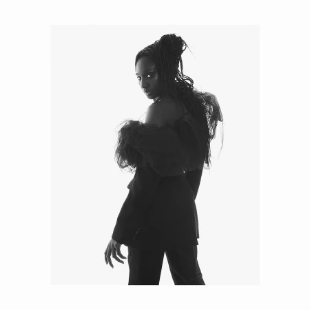 Black and white portrait of a woman with braided hair wearing a dark textured top against a white background