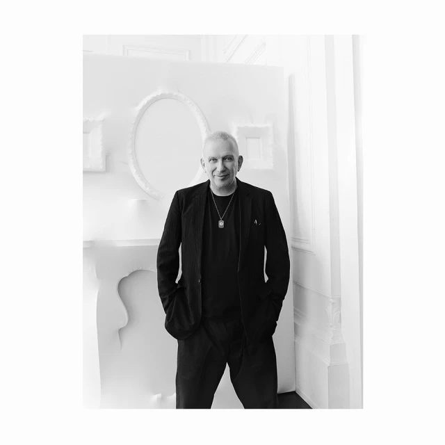 Black and white portrait of a mature Caucasian male in a suit with a white backdrop and a decorative plaster wall.