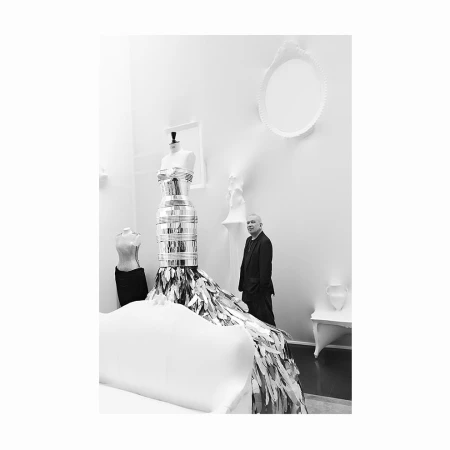 Monochrome interior view featuring a metallic strapless dress on a mannequin and a man standing nearby.