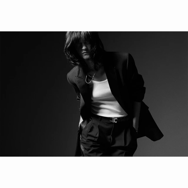 Black and white studio shot of adult female with dark hair wearing an oversized blazer, white top, and dress pants, looking forward.
